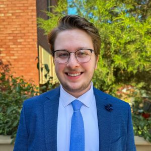 Photo of Ben Rosenstiel wearing a blue dress suit with a blue tie. 