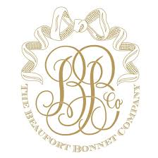 The Beaufort Bonnet Company logo consists of a white background with a long gold ribbon (top) and the capitalized gold text "THE BEAUFORT BONNET COMPANY" on the bottom, which forms a U shape. Together the ribbon and text form a circle shape. Inside the ribbon and text circle are two gold cursive B's with the gold word "Co" on the inside of the right side of the second b (bottom part of the second loop in the b).