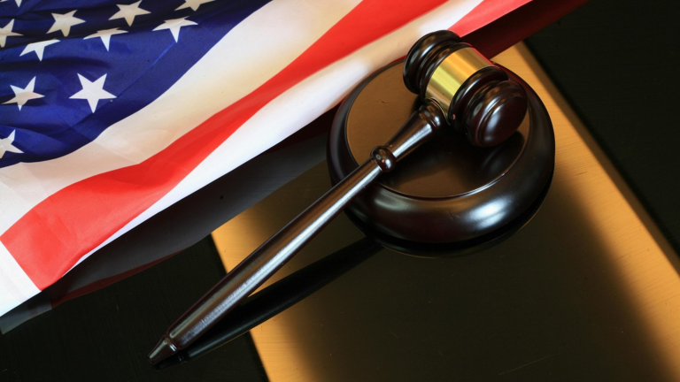 A gavel on a shiny table with an American flag lying down next to it.
