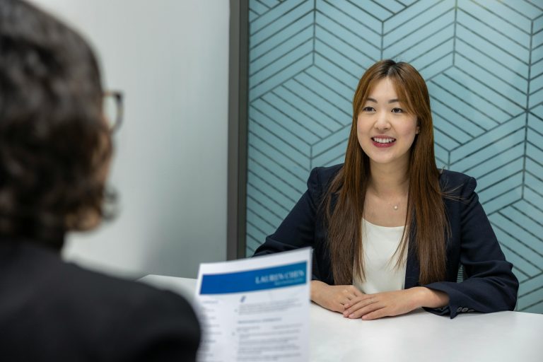 A young and confident-looking woman being interviewed for a new job. The location is in a modern-looking office.