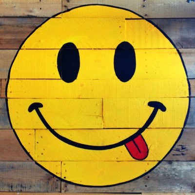 SkinnyFATS company logo consists of a yellow smiley face with its tongue sticking out to the side of its mouth. IT appears the smiley face was painted on horizontal wood planks.