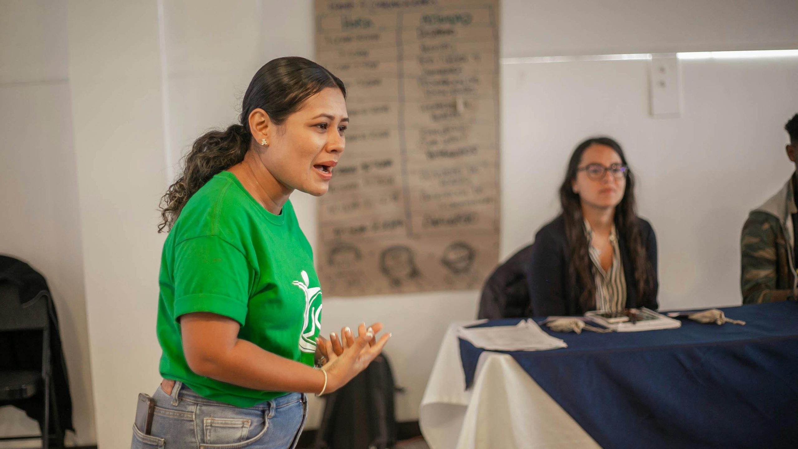 Woman wearing a green t-shirt with a nonprofit logo on it speaking to an audience.