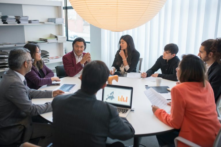People sitting at a round table with their laptops, notes, and phones.