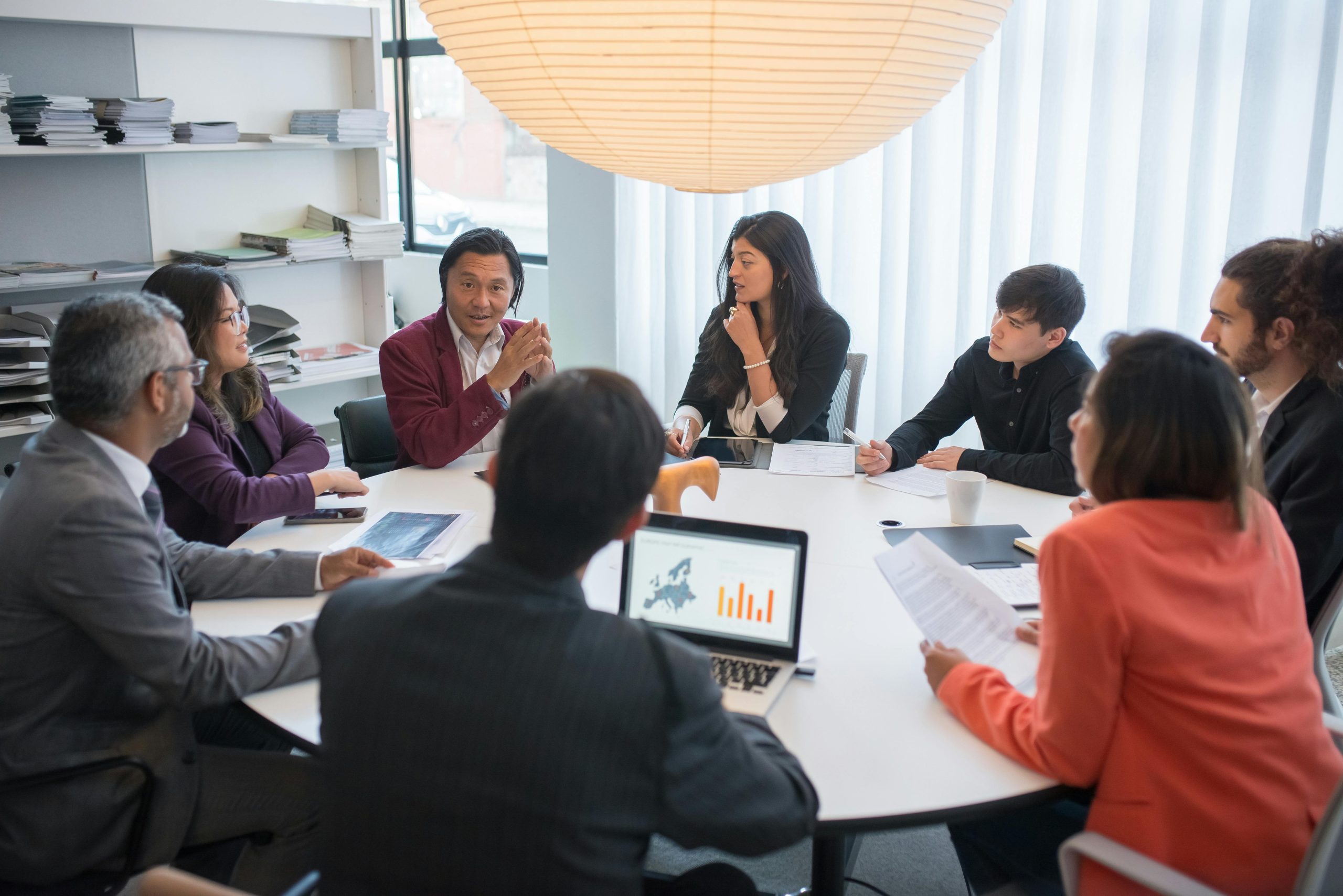 People sitting at a round table with their laptops, notes, and phones.