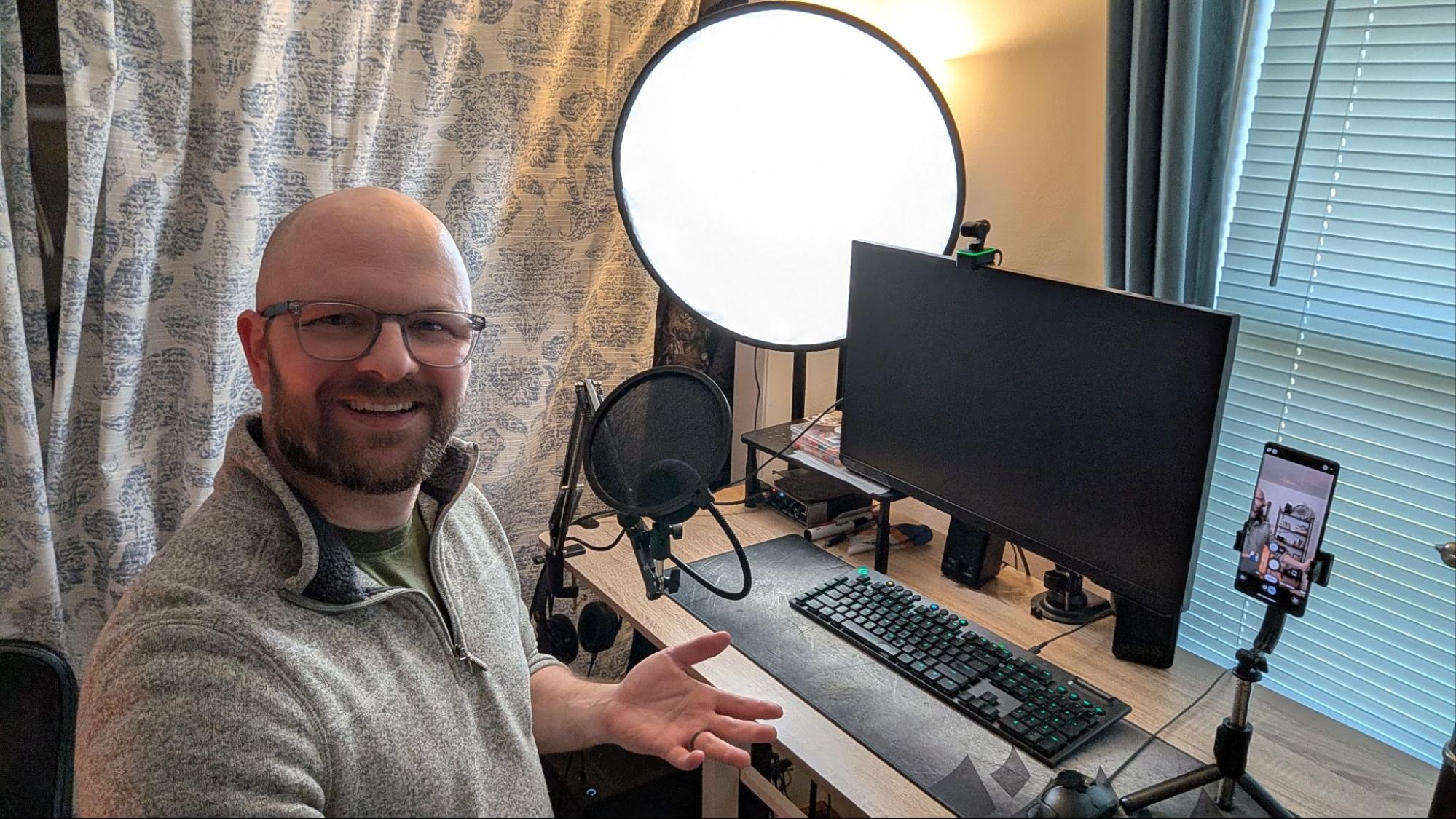 Justing smiling at the camera and showing a large, round, white light on his desk by his computer.
